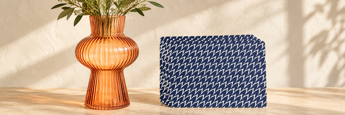 Large Amber Shapely Fluted Glass Vase and Leaf Placemats Dark Blue Set Of Four arranged in a warm, softly lit setting.