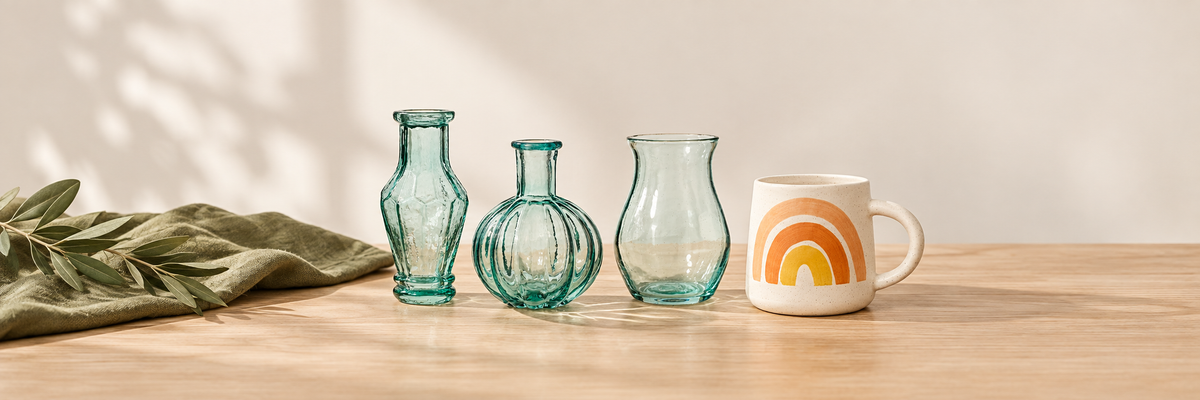 Green glass bud vases and a rainbow ceramic mug on a wooden table