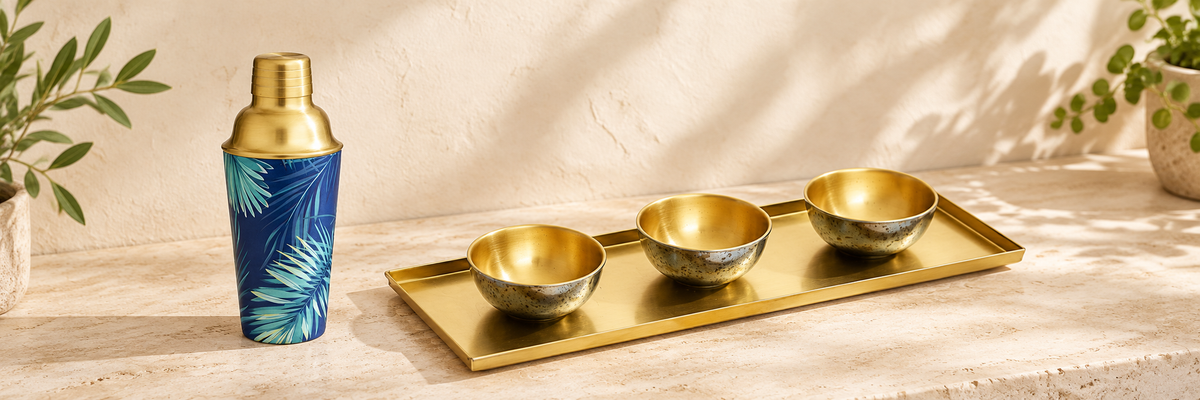 Tropical Palm Leaf Cocktail Shaker - Brass and Hammered Brass Platter & 3 Serving Bowls arranged in a warm, softly lit setting.