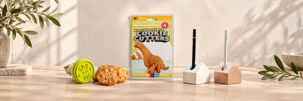 Cookie stamp, dinosaur cookie cutters and house-shaped pen holders on a pale wooden table