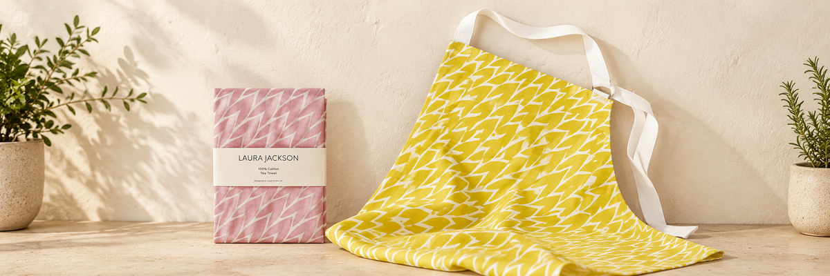 Leaf Cotton Tea Towel - Pink and Leaf Cotton Apron - Yellow arranged in a warm, softly lit setting.
