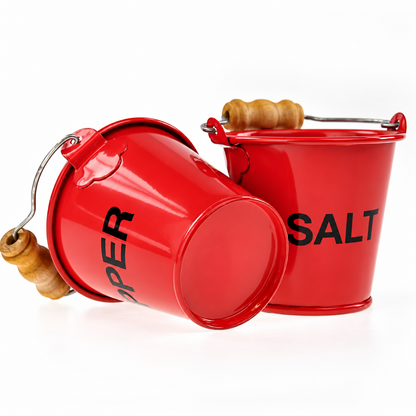 Red pepper fire bucket resting on its side beside an upright salt bucket, showing the metal base and wooden handles